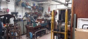 205Cf0F8 Fd03 4A12 A222 64Ed032F83Ea Industrial Clearance A messy workbench in a workshop or garage, covered with various tools, machinery, metal components, vices, and containers, awaiting a thorough industrial workshop clearance.