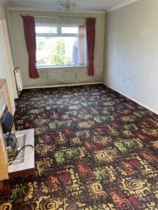 House Clearance Birmingham10 Garden Clearance A spacious, empty living room with an old, brightly patterned carpet and a window, demonstrating a room that has been partially cleared during a house clearance process.