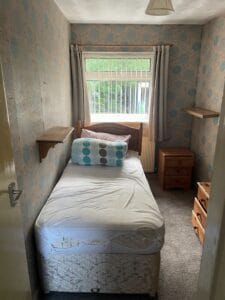 House Clearance Birmingham5 Garden Clearance A small bedroom with a single bed, bedside tables, and patterned wallpaper, ready for full house clearance and removal of furniture.