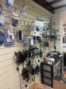 Retail Shop Clearance West Midlands3 Retail Shop Clearance A close-up of a shop wall (slatwall) covered in dozens of tangled black and white computer cables and chargers hanging from hooks. Several packaged electronics, including a boxed keyboard, are also hanging, indicating a messy inventory clearance is underway.