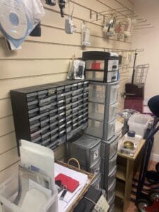 Retail Shop Clearance West Midlands5 Retail Shop Clearance A corner of an electronics shop showing two large, dark plastic storage units. One unit has dozens of small drawers for tiny components (likely screws, resistors, or small parts). The other unit is stacked plastic drawers holding various cables and electronic accessories. The walls are lined with beige slatwall.