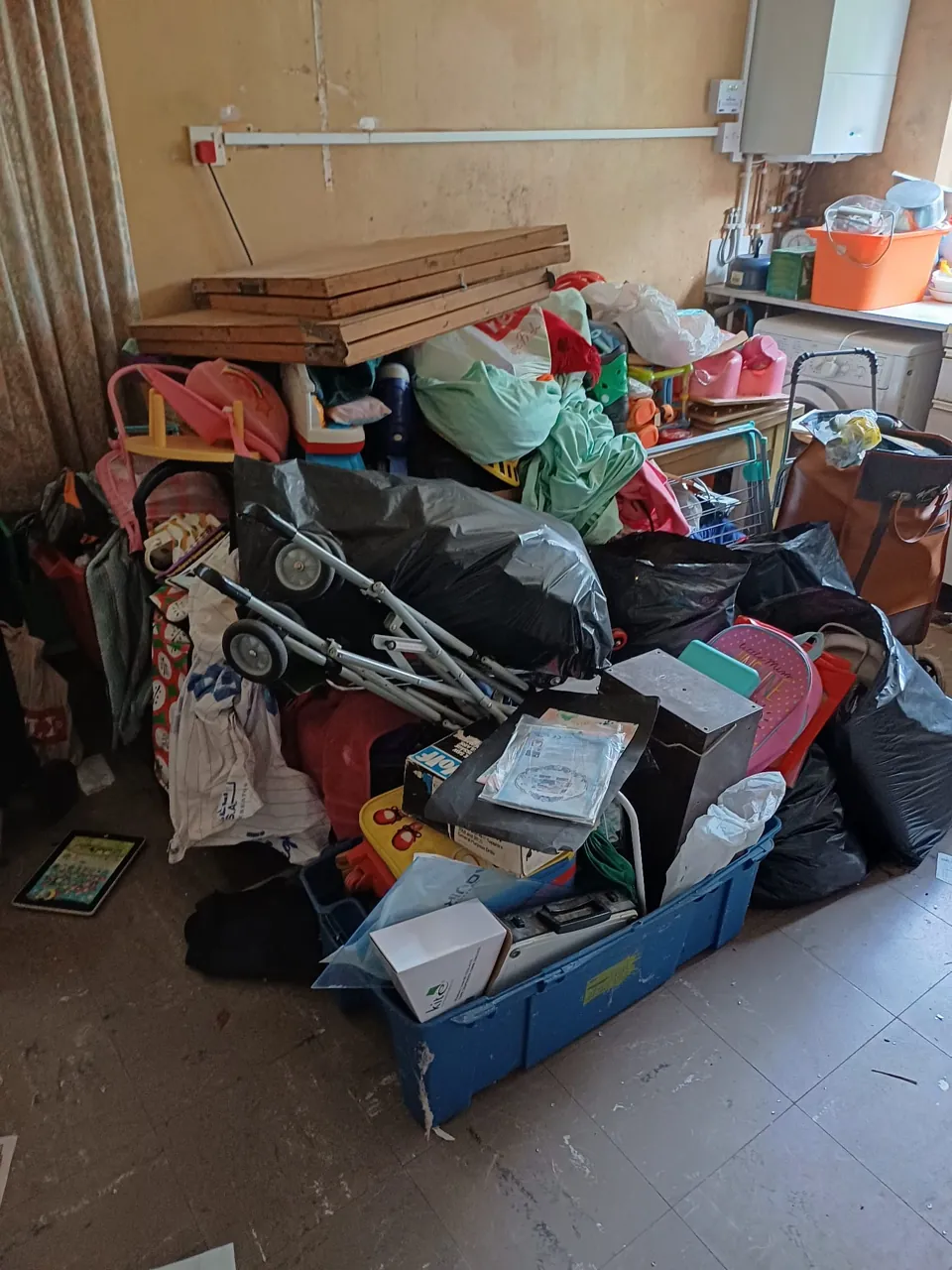 Kitchen floor piled with bags, boxes, a pushchair and household items awaiting clearance